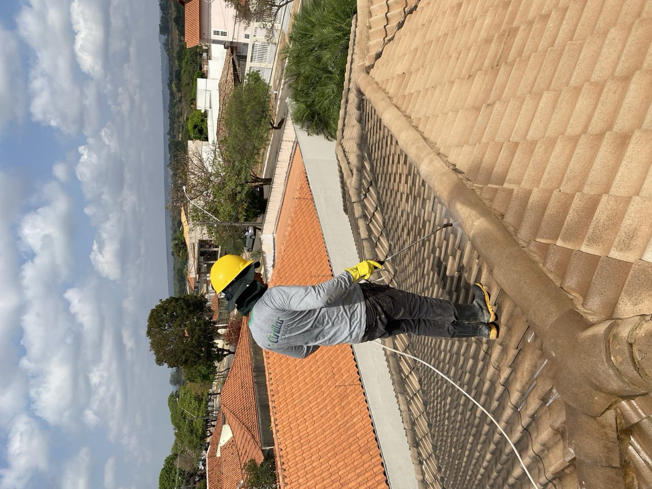 Profissional Cintilar com equipamento de segurança higienizando telhado cerâmico em altura